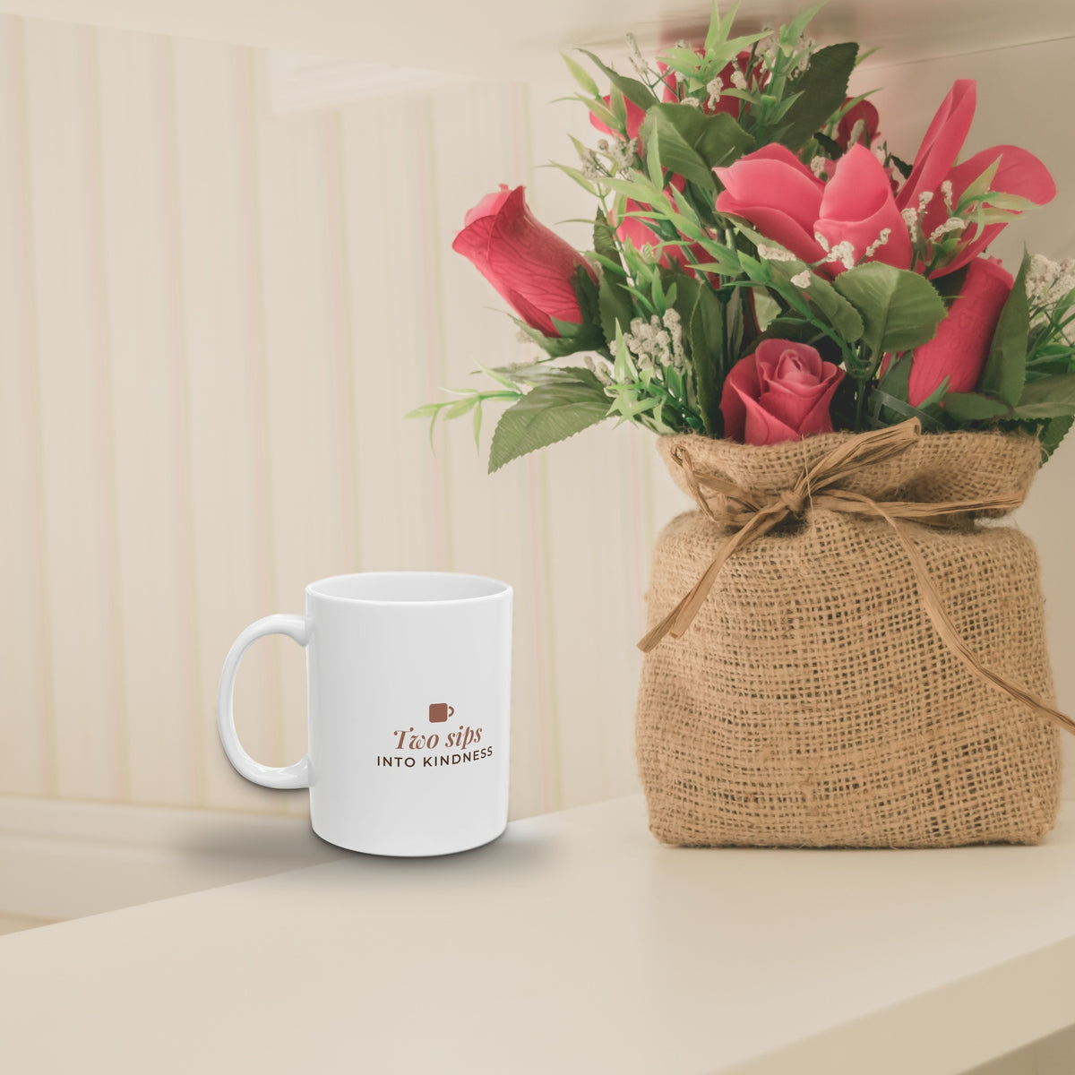 Two Sips Into Kindness mug on a shelf beside flowers