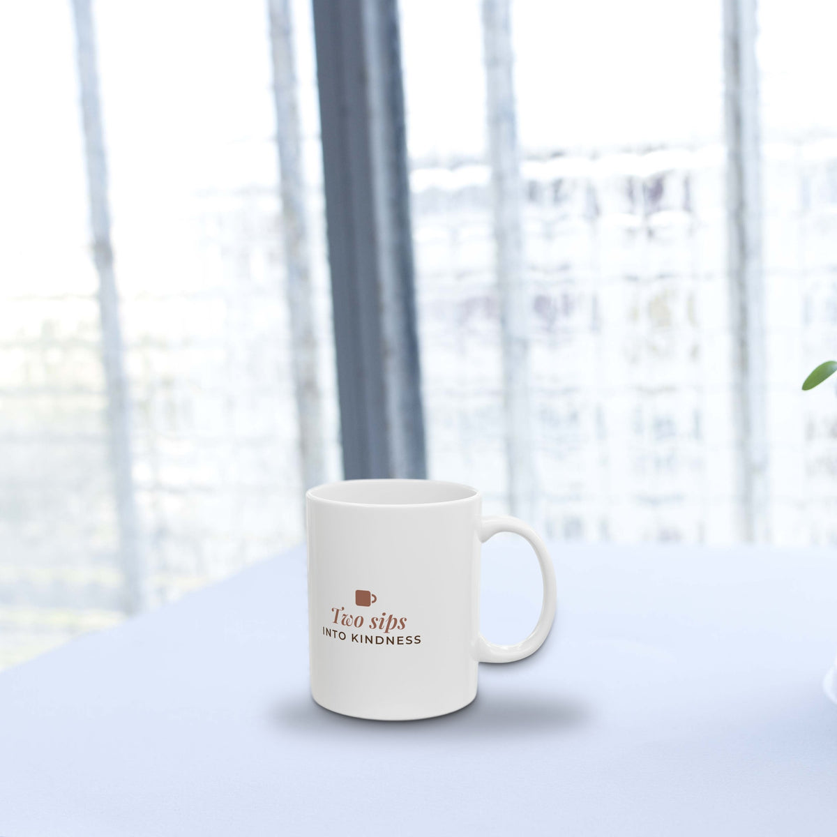 Two Sips Into Kindness mug on a bright white table by a window