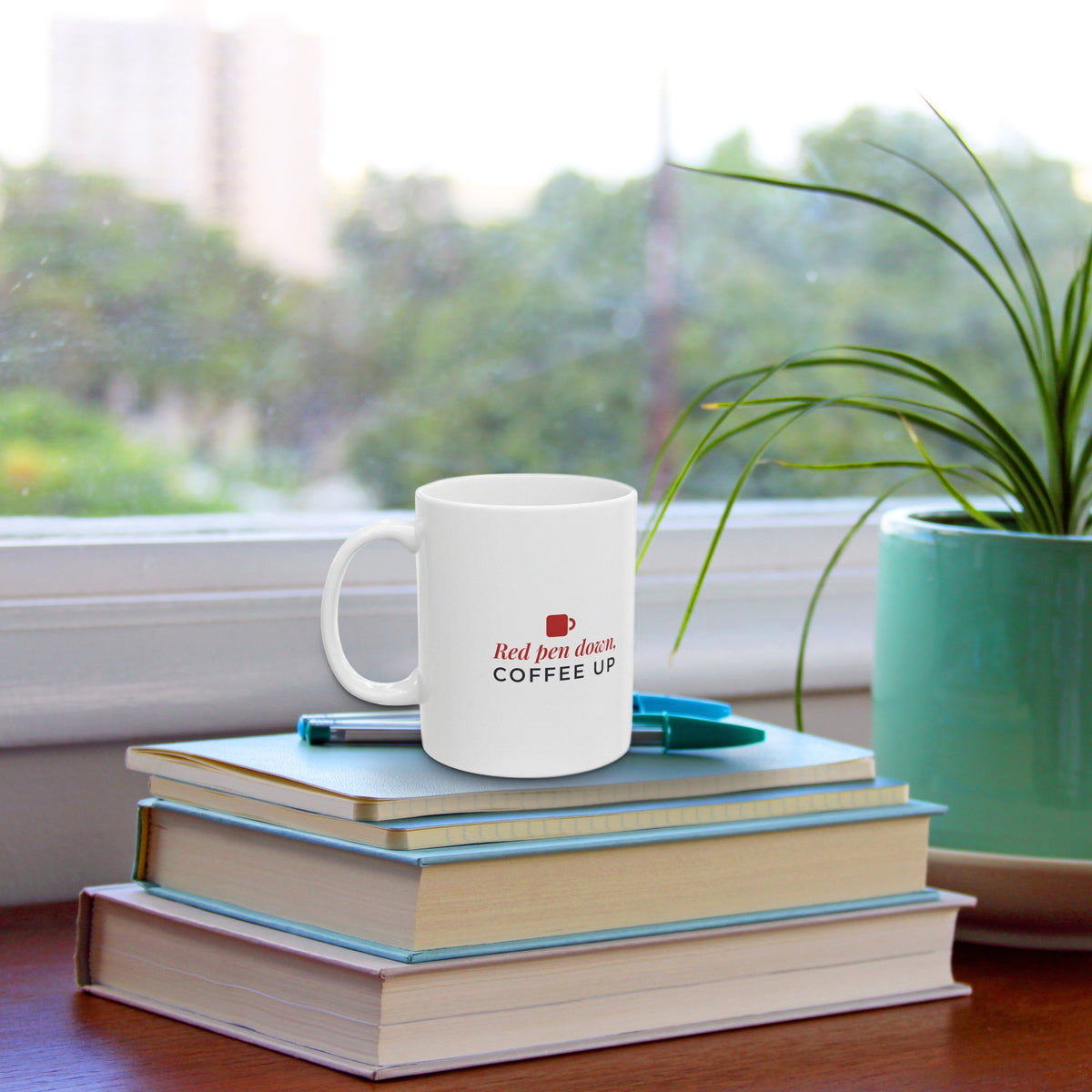 Red Pen Down Coffee Up mug on a stack of books by a sunny window