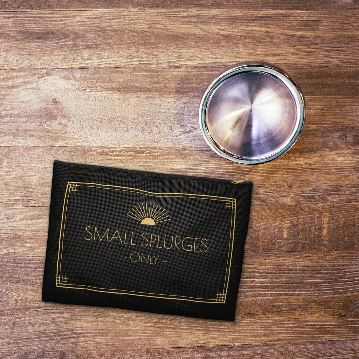 Small Splurges Only black art deco pouch on a wooden table beside a glass